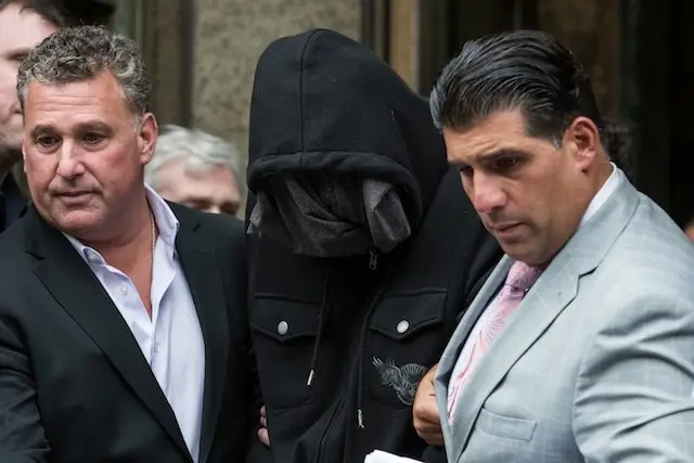 A hooded Detective Wojciech Braszczok being led out of his arraignment in 2013 with his defense attorney, John Arlia, at right